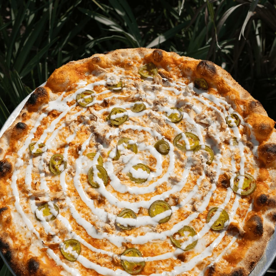 A Pizza by the Sea pizza with chicken, jalapeños, and a spiral of white sauce.
