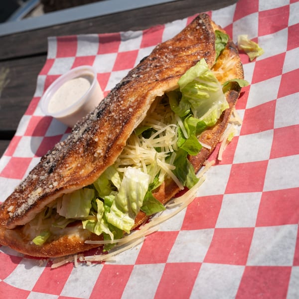A calzone filled with fresh green lettuce and shredded cheese, served with a side of dressing.