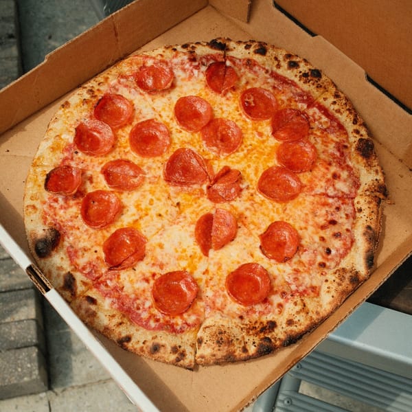 A freshly baked pepperoni pizza from Pizza by the Sea, in an open cardboard delivery box.