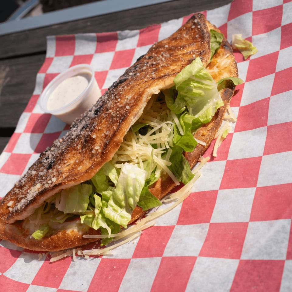 A Pizza by the Sea calzone filled with fresh lettuce and shredded cheese, served with a side of dressing.
