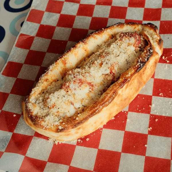 A baked calzone or stromboli filled with cheese and sauce, topped with parmesan, on checkered paper.