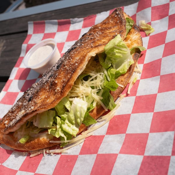 Pizza by the Sea's Caesar salad calzone, filled with lettuce and cheese, served with dressing.