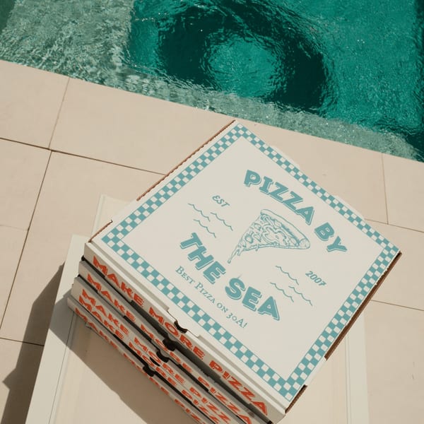Stack of Pizza by the Sea pizza boxes with a blue and white checkered design next to a pool.