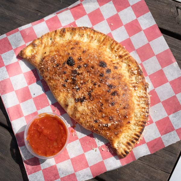 Golden-brown calzone with parmesan and a side of marinara sauce on red and white checkered paper.