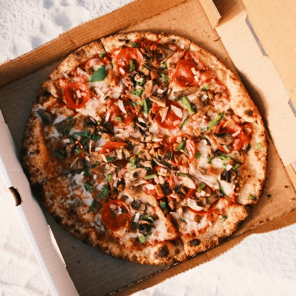 A Pizza by the Sea pizza, topped with pepperoni, mushrooms, green peppers, and onions, in a cardboard box.