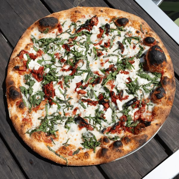 Pizza by the Sea's white pizza with sun-dried tomatoes, ricotta, and basil on a wooden table.